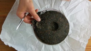 Shu Puerh keki Çin mayalanmış siyah çayı beyaz kağıtta bıçakla. Erkek ellerinin elinde çip kırıkları eski yuvarlak, olgunlaşmış siyah pu-erh parçaları. Sağlıklı canlandırıcı içecekler..