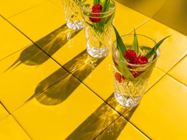 Yeşil yapraklı, ahududu sarısı fayans arkaplan gölgeli kristal bardaklarda ferahlatıcı yaz içkileri. Tatlı soğuk doğal kokteyl sıcak yaz günü. Soda, meyve, nane şurubu. Parti tatili