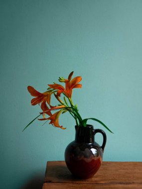 Kaplan zambağı seramik vazoda gölgeli turkuaz duvar arka planında. Lilium lancifolium portakal çiçeği buketi ahşap çiftlik masasında. Yazlık kır evi estetiği ülke kırsal minimalizm karanlık stil.