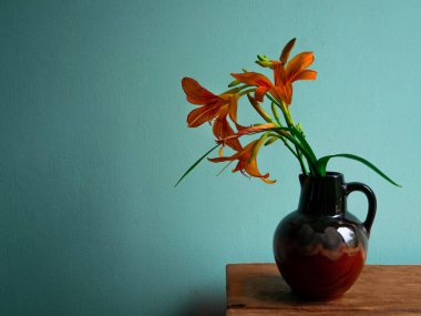 Kaplan zambağı seramik vazoda gölgeli turkuaz duvar arka planında. Lilium lancifolium portakal çiçeği buketi ahşap çiftlik masasında. Yazlık kır evi estetiği ülke kırsal minimalizm karanlık stil.