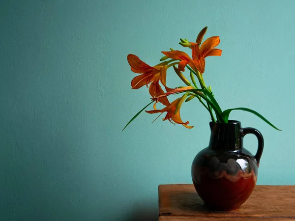 Tiger lily in ceramic vase with shadow turquoise wall background. Lilium lancifolium orange flowers bouquet on wooden farmhouse table. Summer cottagecore aesthetic country rural minimalism dark style.
