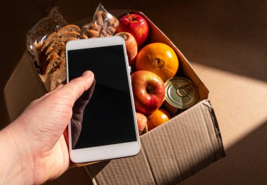 Sağlıklı yemek teslimatı akıllı telefon dokunmatik ekran modeli el şablonunda. Ürün paketini kaldırın. Yeni normal süpermarket online alışveriş restoranı teslimat konsepti. Meyve sebzeli kahvaltı menüsü.