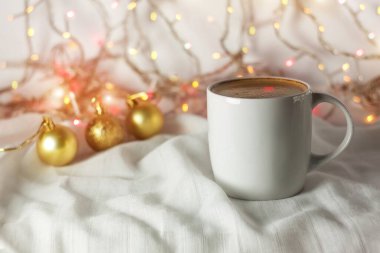 Noel kahvesi fincanı, altın süslemeler, arka plan ışıkları. Sıcak içecek tasarımı sunum şablonu olan beyaz bardak. Kış tatili tebrik kartı konsepti. Mekanı kopyala.