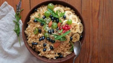 Taze böğürtlenli tam tahıllı yulaf lapası, nane fıstığı kadın elinde susam tohumu. Sağlıklı yemek yulaf ezmesi kahvaltı manzarası. Tam tahıllı tahıl gevreği üzümlü üzümlü üzümlü muz ahşap masa.