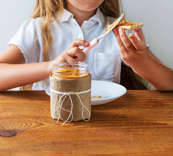 Barn Äter Knäckebröd Med Jordnötssmör Som Sitter Vid Bordet Hemma — Stockfoto