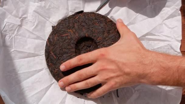 舒淇梨ケーキ中国のナイフで白い紙に紅茶発酵 男性の手は チップブレークを保持している部分に暗いPu Erh熟した古いラウンドフォームを押圧健康的な爽快なドリンクコーヒー代わりに4K — ストック動画