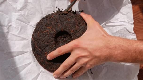 舒淇梨ケーキ中国のナイフで白い紙に紅茶発酵 男性の手は チップブレークを保持している部分に暗いPu Erh熟した古いラウンドフォームを押圧健康的な爽快なドリンクコーヒー代わりに4K — ストック動画