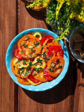 Sarı kırmızı domates ve mavi kâse kahvaltı manzaralı tatlı biber salatası. Taze çiçek ve renkli sebzeler dilimlenmiş yeşillikler zeytin yağı sirkesi kabağı tahtadan sehpada susam tohumları