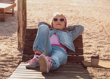 Plaj sandalyesinde dinlenen küçük bir kız. Mutlu çocuk gülümsüyor, rahatlıyor, hayatın tadını çıkarıyor, temiz hava alıyor. Hayat tarzı seyahat gerçek insanlar dışarıda. İyi tatiller. Özgürlük mutluluk mesafesi e-öğrenme.