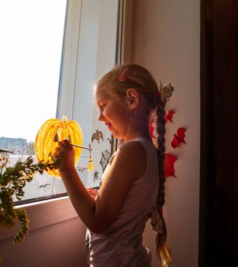Pencereye balkabağı çizen çocuk Cadılar Bayramı 'nı kutlamaya hazırlanıyor. Küçük kız odasını kağıt yarasalarla süslüyor ve sonbahar tatilini evde kutluyor. Yaratıcı aile eğlencesi yeni gerçeklik kilitlenmesi