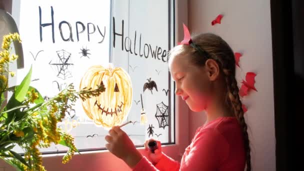 窓の上にカボチャを描いた悪魔の角の子供はハロウィンを祝います 小さな子供が部屋の内装紙のコウモリを描くお祝い秋の休日の家創造的なレジャーロックダウン新しい現実 — ストック動画
