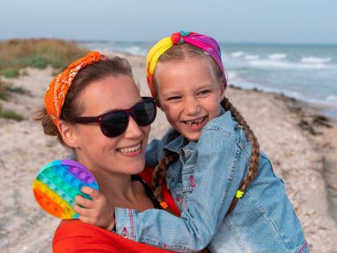 Neşeli anne ve kızı deniz sahilinde yürürken gülümsüyor. Mutlu bir aile. Gökkuşağı oynayan sevimli küçük çocuk dışarıda oyna. Anneler Günün kutlu olsun. Anneliğin neşesi Ebeveynler mutluluk bakımı kavramını sever