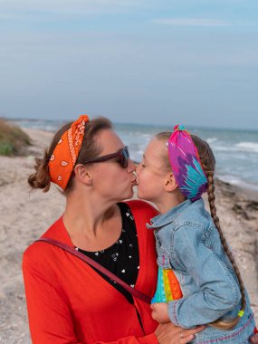 Neşeli anne ve kızı deniz sahilinde yürürken gülümsüyor. Mutlu bir aile. Gökkuşağı oynayan sevimli küçük çocuk dışarıda oyna. Anneler Günün kutlu olsun. Anneliğin neşesi Ebeveynler mutluluk bakımı kavramını sever