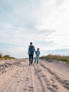 Mutlu baba-kız koşuyor ve boş sonbahar deniz sahillerinde eğleniyorlar. Baba ve çocuk, mavi gökyüzü arka planına sahip beyaz kumlu yolda yürüyorlar. Yaşam tarzı gerçek insanlar. Mutluluk yolculuğu konsepti
