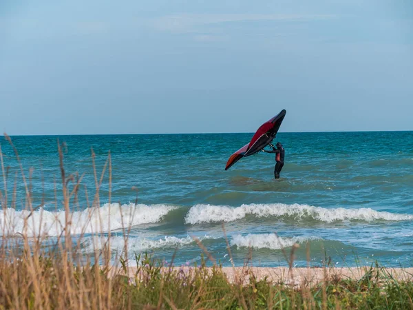 The athlete riding a hydrofoil surfboard using a hand held foil wing on ocean waves. Autumn extreme sport. Fall sea vacation fun. Windy weather on the beach.