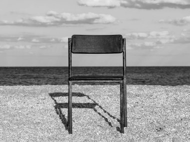 Mavi deniz suyu arka planına sahip boş kumsal sahilinde siyah plaj sandalyesi. Minimalizm tarzı sonbahar seyahati rahatlama, sonbahar tatili. Kimse yok, içe dönük psikoloji melankoli depresyonu