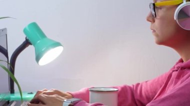 Kulaklık takan, ev uzaklığı öğrenme bürosundan dizüstü bilgisayarda çalışan serbest çalışan bir kadın. Kahve içen güzel kız internette video konferansı dinliyor. Gözlüklü kadın..