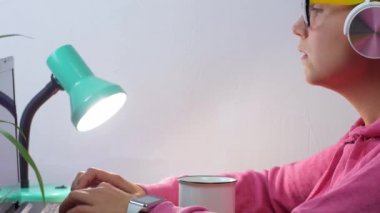 Kulaklık takan, ev uzaklığı öğrenme bürosundan dizüstü bilgisayarda çalışan serbest çalışan bir kadın. Kahve içen güzel kız internette video konferansı dinliyor. Gözlüklü kadın..