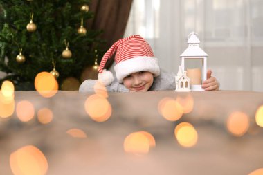 Kırmızı beyaz bir yeni yıl şapkası takmış bir çocuk avucunun üzerine uzanmış, elinde bir lambayla kocaman dudaklarıyla gülümsüyor. Noel ağacının yanında, sıcak, yuvarlak ışıklar altında.. 