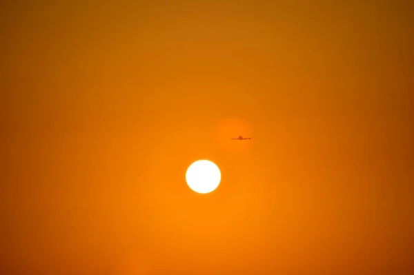 El avión está ganando altitud, con alas uniformemente extendidas. Moscas en naranja puesta de sol en el punto de reflexión. — Foto de Stock