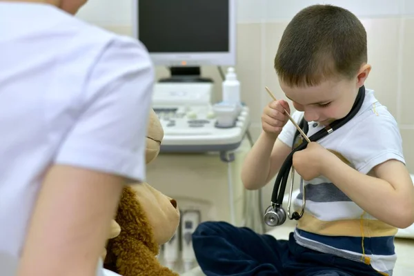 Doktor ve bir çocuk, başı cebine eğilmiş bir şekilde tıbbi bir spatula yerleştirir. Muayene için klinikte.. — Stok fotoğraf