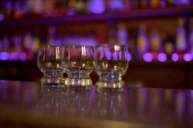 Üç küçük cam bardak, barın üstünde, mor ışıkların ışığında.. 