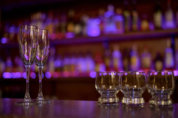 2つのワイングラスにはライトと3つの小さなスピリッツグラスが紫色の輝きで満たされています. — ストック写真