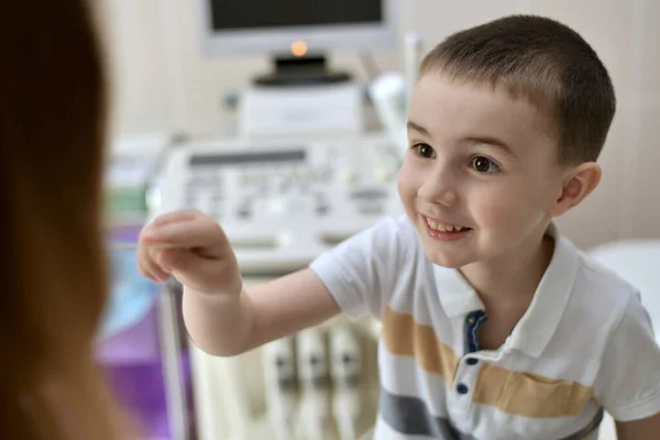 幸せな茶色の目の子供は 背景に超音波マシンでオフィスでへらで医者を治療します 診療所で受付で — ストック写真