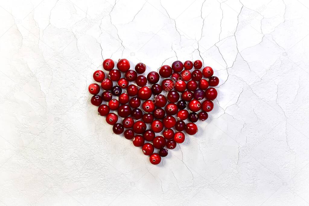 The heart is laid out, large in the center, with red glossy cranberries. On a white background with cracks and a rough matte texture.