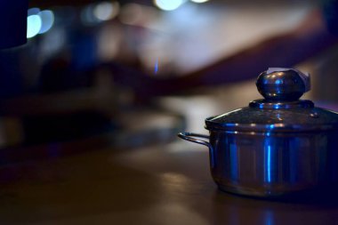 Masanın üzerinde duran cam kapaklı çelikten küçük bir tava akşam vakti, bir yemek restoranında, kahverengi tonlu sıcak bir fonda tek başına duruyor..
