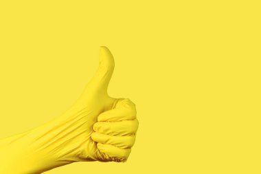 Bir elin hareketi, bir yumruğa yapışmış, gerilmiş, sarı bir nitrile sarılı bir başparmak ile aynı renkte bir arka plana karşı aydınlatıcı eldiven..