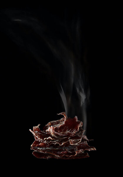  Dried deer meat. Thin planks with curled edges, shaped like a pyramid, and a plume of smoke, on a black vertically.
