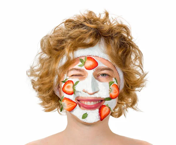 Portrait d'une fille bouclée aux cheveux roux souriant avec un masque cosmétique sur son visage. Photo De Stock