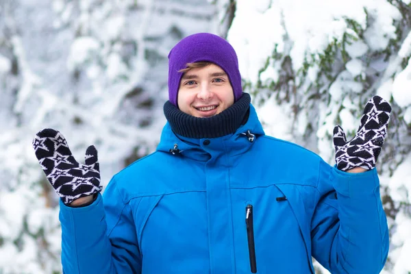 Retrato de un joven y guapo hombre feliz con ropa de abrigo, suéter y sombrero caminando en un bosque frío de invierno. El tipo positivo está mirando a la cámara y sonriendo al aire libre — Foto de Stock