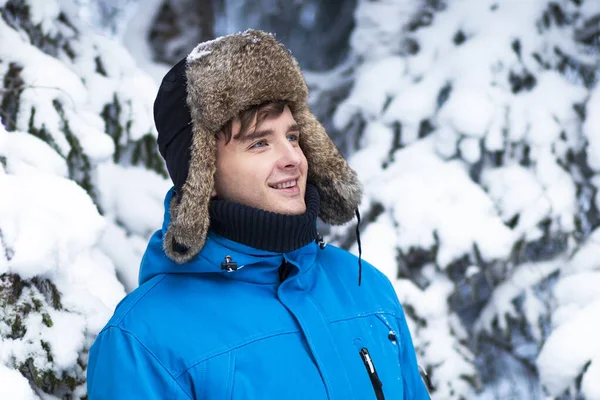 一个穿着冬衣、头戴耳罩的英俊而快乐的年轻人的画像。他面带微笑，享受着冬天的好天气和寒冷的雪天 — 图库照片