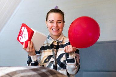 El ele tutuşan heyecanlı kızın portresi hediye kutusu ve kırmızı balon. Genç ve güzel bir kadın Sevgililer Günü hediyesi aldı. Evinde mutlu ve gülümsüyor.