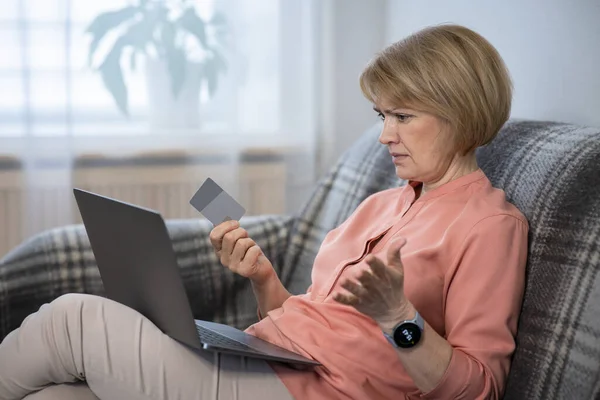 Nervous confused senior woman, stressed worried angry lady having problem with paying, buying online, payments with credit blocked bank card, looking at screen, monitor of laptop. Internet fraud