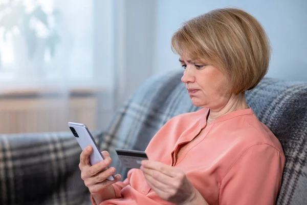 Nervous confused elderly senior woman, stressed worried sad frustrated lady having problem with paying, buying online, payments with credit blocked bank card, mobile phone, smartphone. Internet fraud