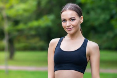 Mutlu, güzel, sağlıklı bir kızın portresi, spor giyimli genç, zayıf spor kadın, açık havada parktaki eğitime gidiyor ve gülümsüyor, kameraya bakıyor.