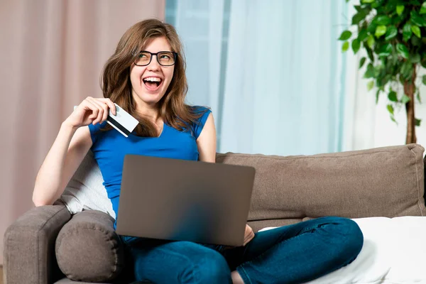 Πορτρέτο ευτυχισμένη θετική ενθουσιασμένοι κορίτσι, νεαρή χαρούμενη χαρούμενη γυναίκα κάθεται στον καναπέ ή καναπέ στο σαλόνι, χρησιμοποιώντας φορητό υπολογιστή, αγοράζοντας με πιστωτική κάρτα τράπεζα, χαμογελώντας. Online αγορές στο διαδίκτυο — Φωτογραφία Αρχείου