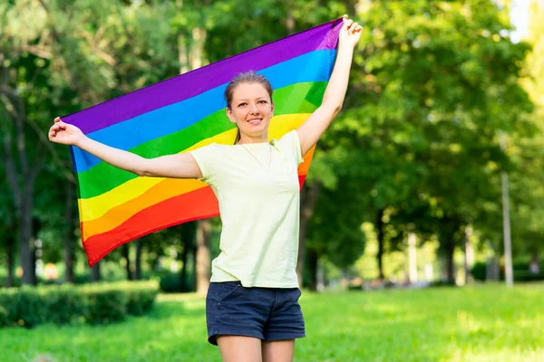 Retrato de joven lesbiana feliz orgullosa mujer, hermosa chica está ondeando arco iris LGBT color gay bandera en verano día soleado sobre fondo natural. Comunidad LGBT, concepto de igualdad de relaciones homosexuales — Foto de Stock