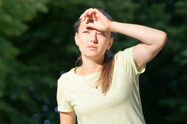 Mädchen leiden unter Schmerzen, Hitze, Frau mit Hitzschlag. Sonnenstich bei sommerlich heißem Wetter. Gefährliche Sonne, Mädchen unter Sonnenschein. Kopfschmerzen, ein schlechtes Gefühl. Person hält Hand auf Kopf. Coronavirus Stockbild