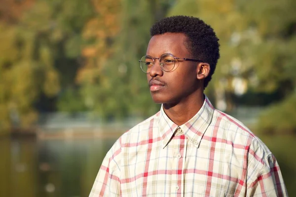 Retrato de homem negro Africano infeliz sério em óculos e camisa. afro americano etnia cara está andando no parque no dourado outono ensolarado dia com desagradável descontente rosto — Fotografia de Stock
