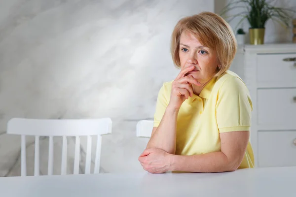 Porträt einer traurig aufgebrachten frustrierten nachdenklichen Frau, ältere Rentnerin sitzt zu Hause am Tisch, hat schlechte depressive Stimmung, Probleme. Stockbild