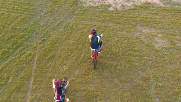 影像B卷4K 航景无人机跟踪年轻人骑自行车在草地上 爱夫妻一起骑自行车在绿色草坪上 空中无人机的视野 健康生活方式概念 — 图库视频影像