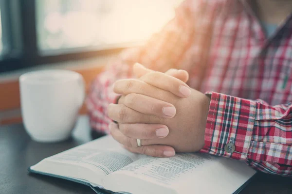 Christian hand while praying and worship for christian religion with blurred of her body background, Casual man praying with her hands together over a closed Bible. christian background. freedom.