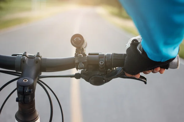 Hands in gloves holding handlebar of a bicycle on road. — Stock Photo, Image