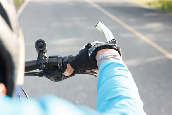 Manos en guantes sosteniendo el manillar de una bicicleta en la carretera . — Foto de Stock