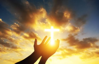 İnsan elleri gün batımında parlayan bir Hristiyan haçına tapınarak avuçlarını açar. İnanç, maneviyat ve umut kavramı.