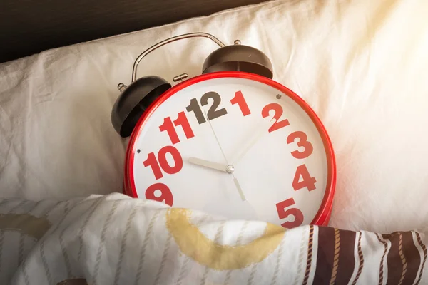 Reloj despertador rojo en la cama con luz solar — Foto de Stock